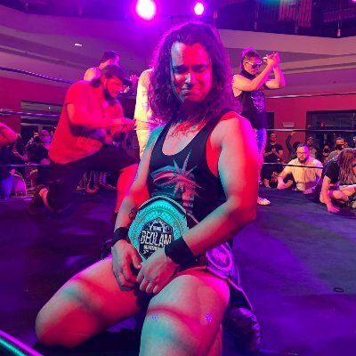 Image: Wrestler Kirby Wackerman in wrestling gear featuring a custom-designed logo, showing off his championship belt.